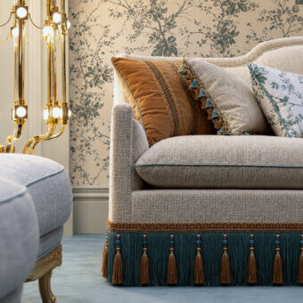 Exclusive Bellotti Ezio 25‑1042 sofa in light gray-beige textured textile with contrasting brown woven band and deep teal fringe studded with gold‑brown tassels, rounded arms and curved back