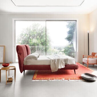 Luxury Noctis Eden Advance bed with curved upholstered headboard, tied bow details, reddish-pink fabric, dark metal legs
