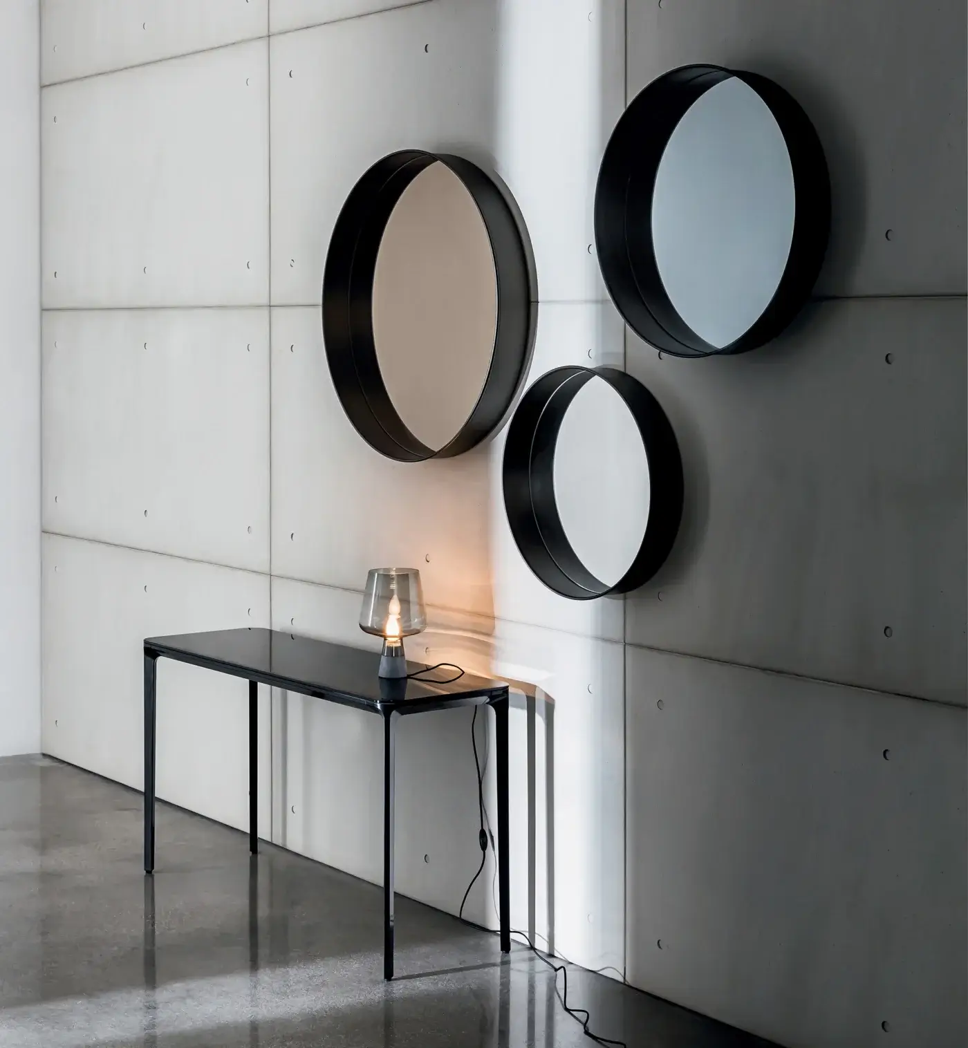 Sovet Italia horizon mirrors, black metal frames, arranged on textured gray wall above black glass console table and brass lamp.