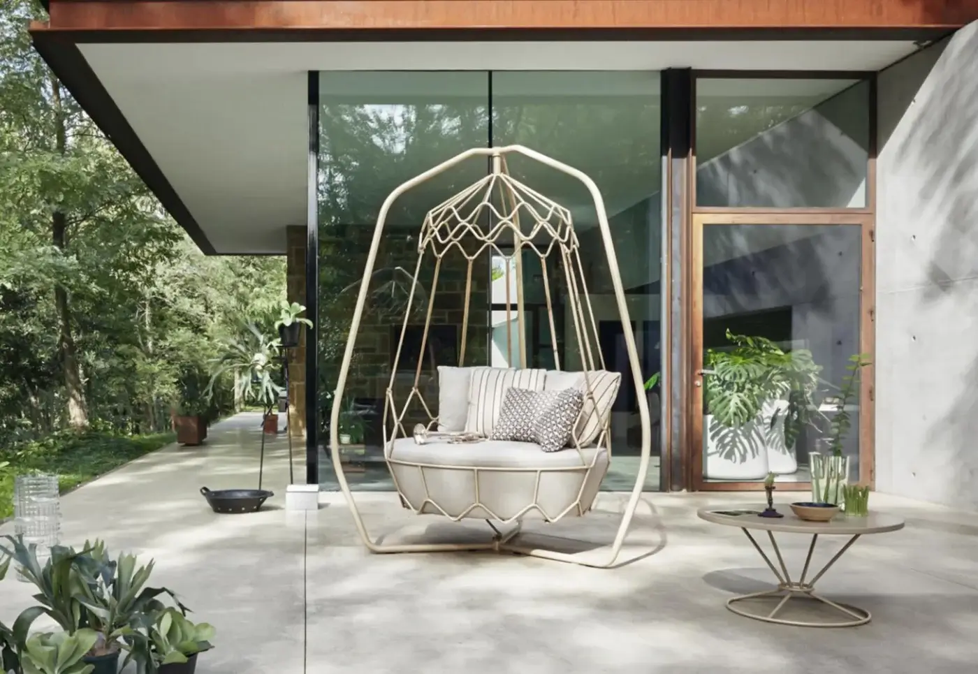 Roberti Rattan lounge chair, white metal frame, arched cage design with neutral cushions on a concrete patio with brass side table.