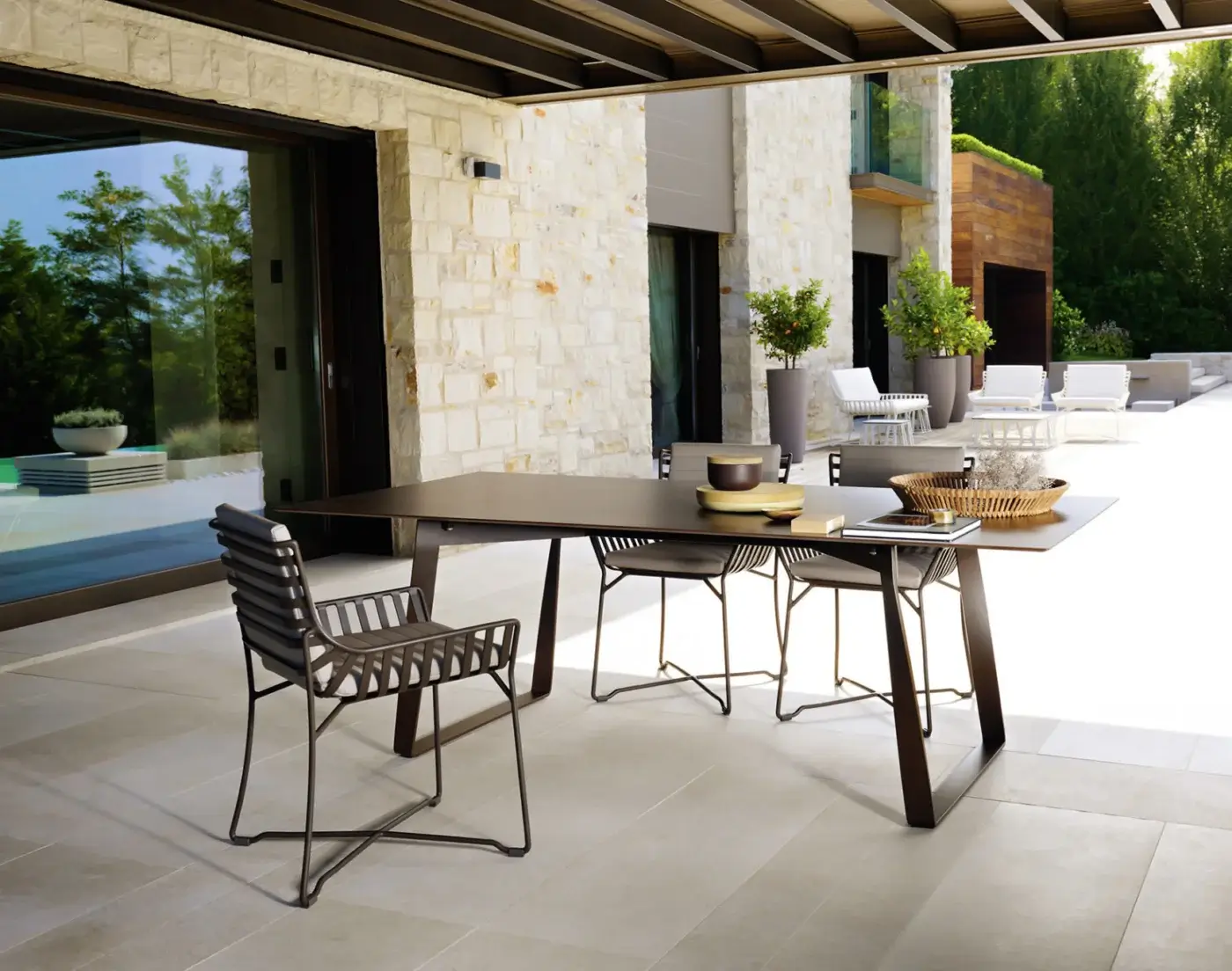 Rattan patio table with dark brown top and angled bronze base, surrounded by four gray woven chairs on a beige tiled patio.
