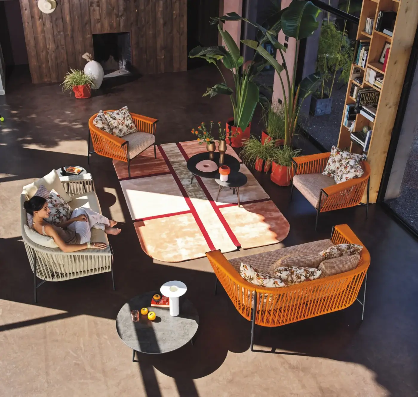 Rattan chairs, orange woven detailing, dark metal legs, arranged around gray marble coffee table in modern living room with plants.