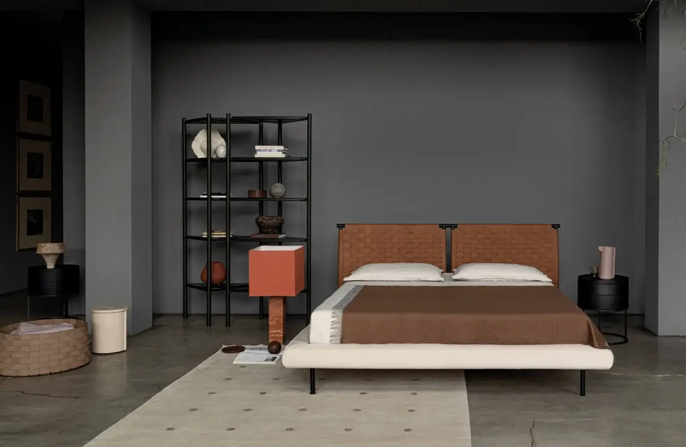Jared bed, dark metal frame, woven leather headboard, warm brown duvet, cream pillows, black metal shelving, terracotta side table, neutral rug.