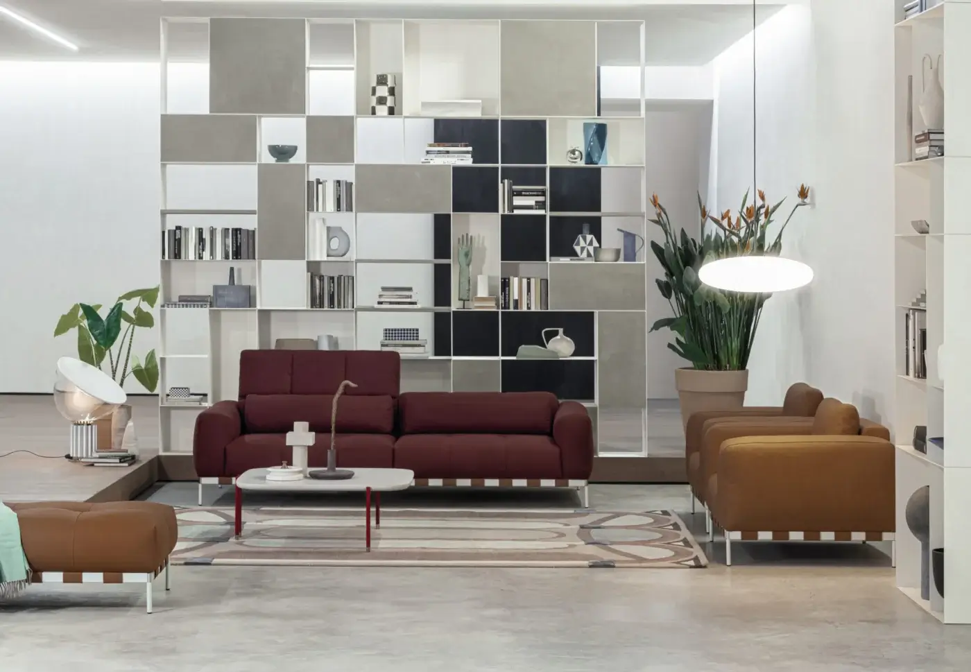 Burgundy Cierre 1972 "Oscar" sofa with squared armrests, light brown leather ottoman, white shelving, and tan leather armchairs in a minimalist room.