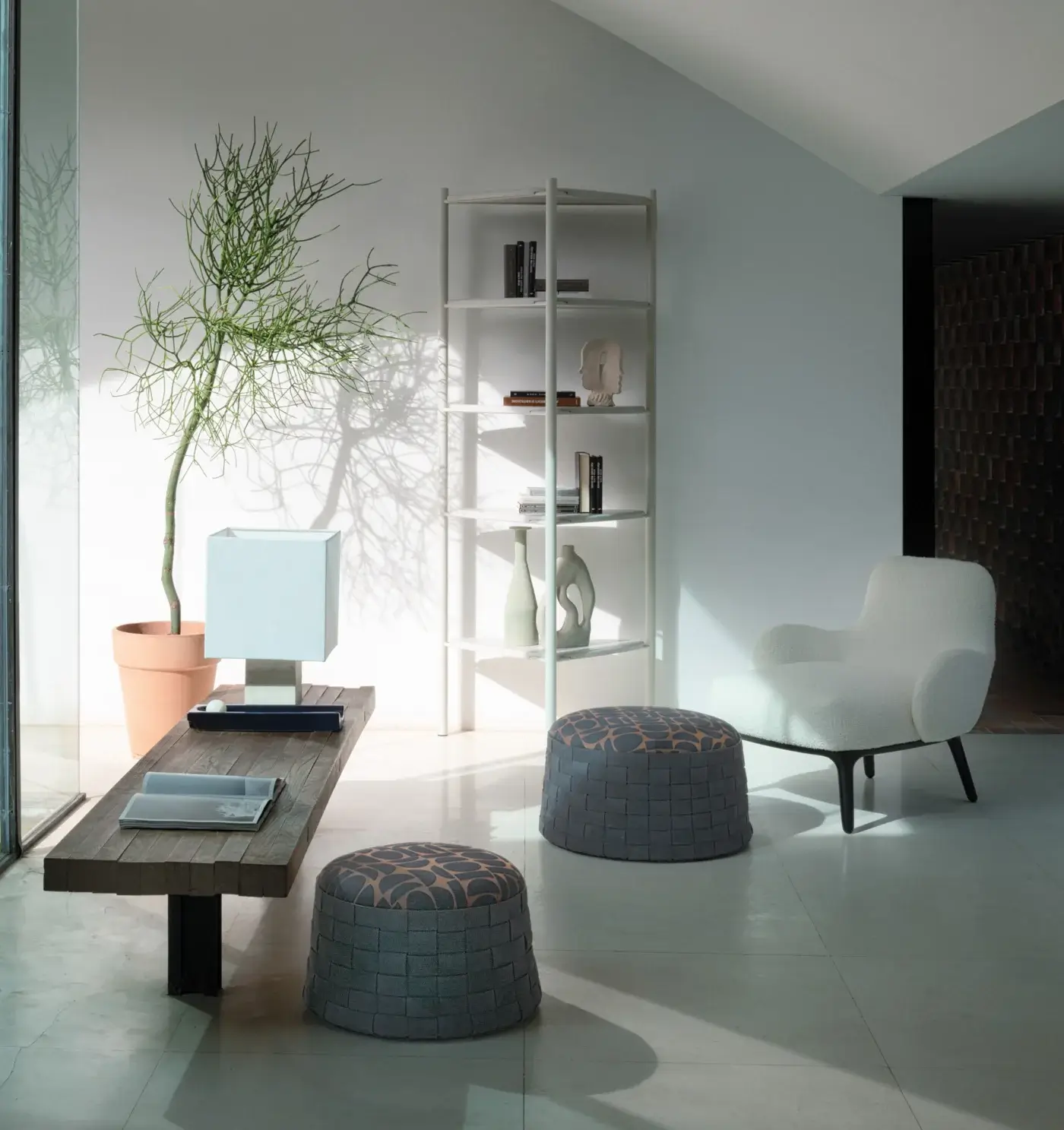 Woody lounge chair, off-white fabric, curved back and armrests, with gray ottoman, wood coffee table, and metal shelving unit.