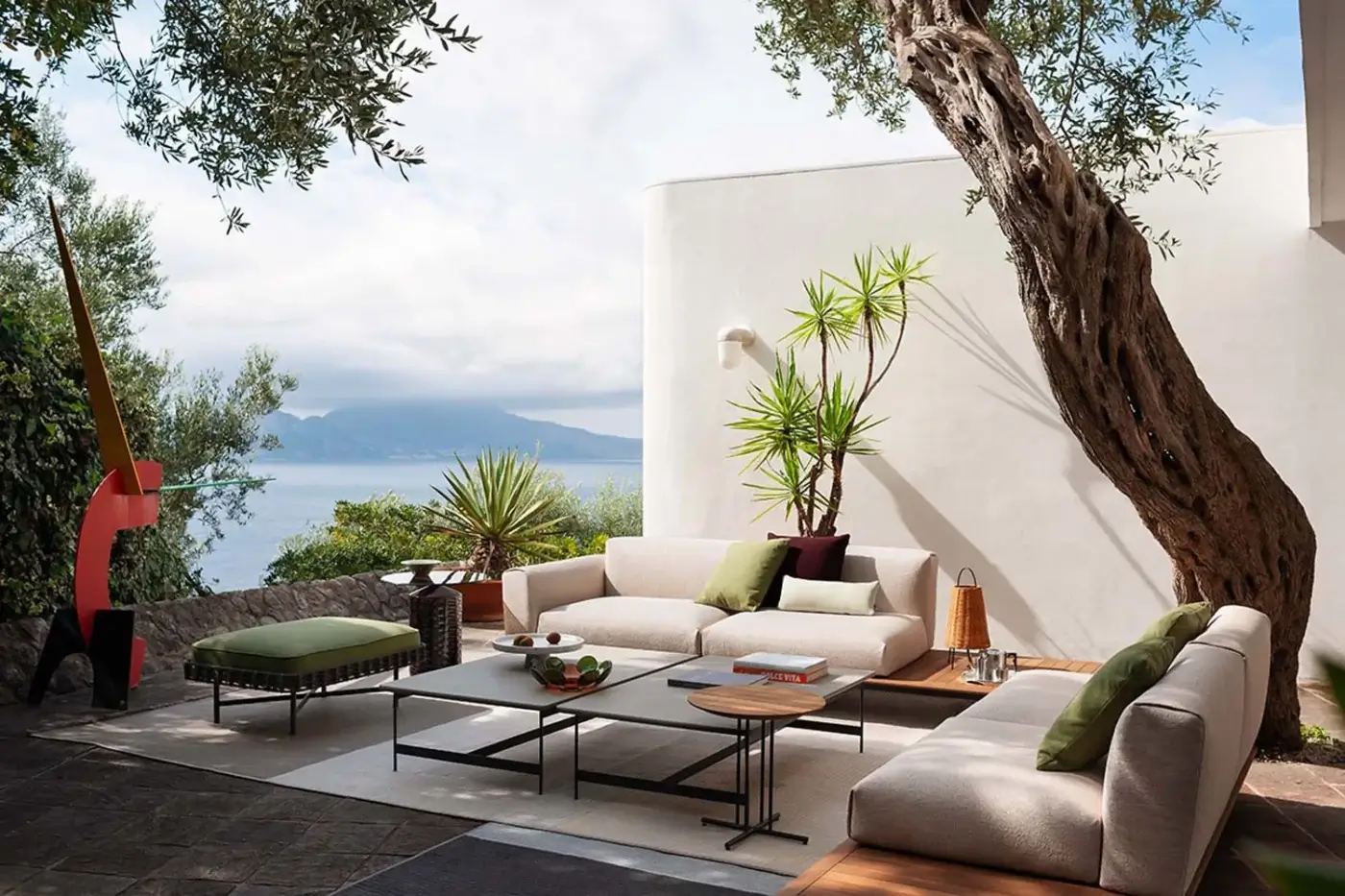 Outdoor sofa by Potocco, beige fabric, modular design with green cushions, dark metal frame on stone terrace with water view.