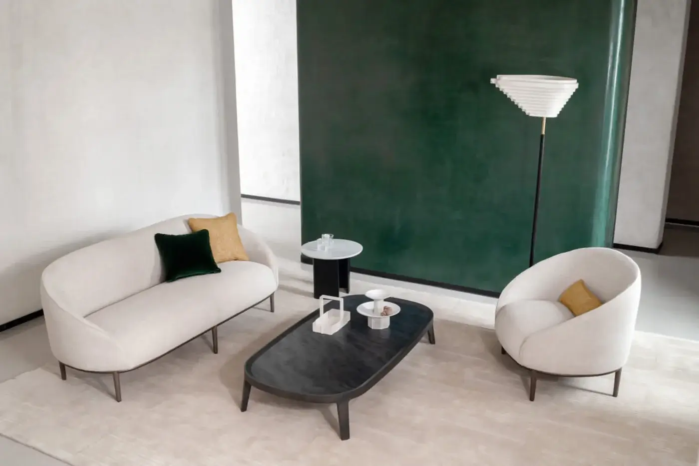 Potocco Yoisho sofa, beige fabric, rounded cocoon shape, with matching armchair, black metal legs, and green wall backdrop.