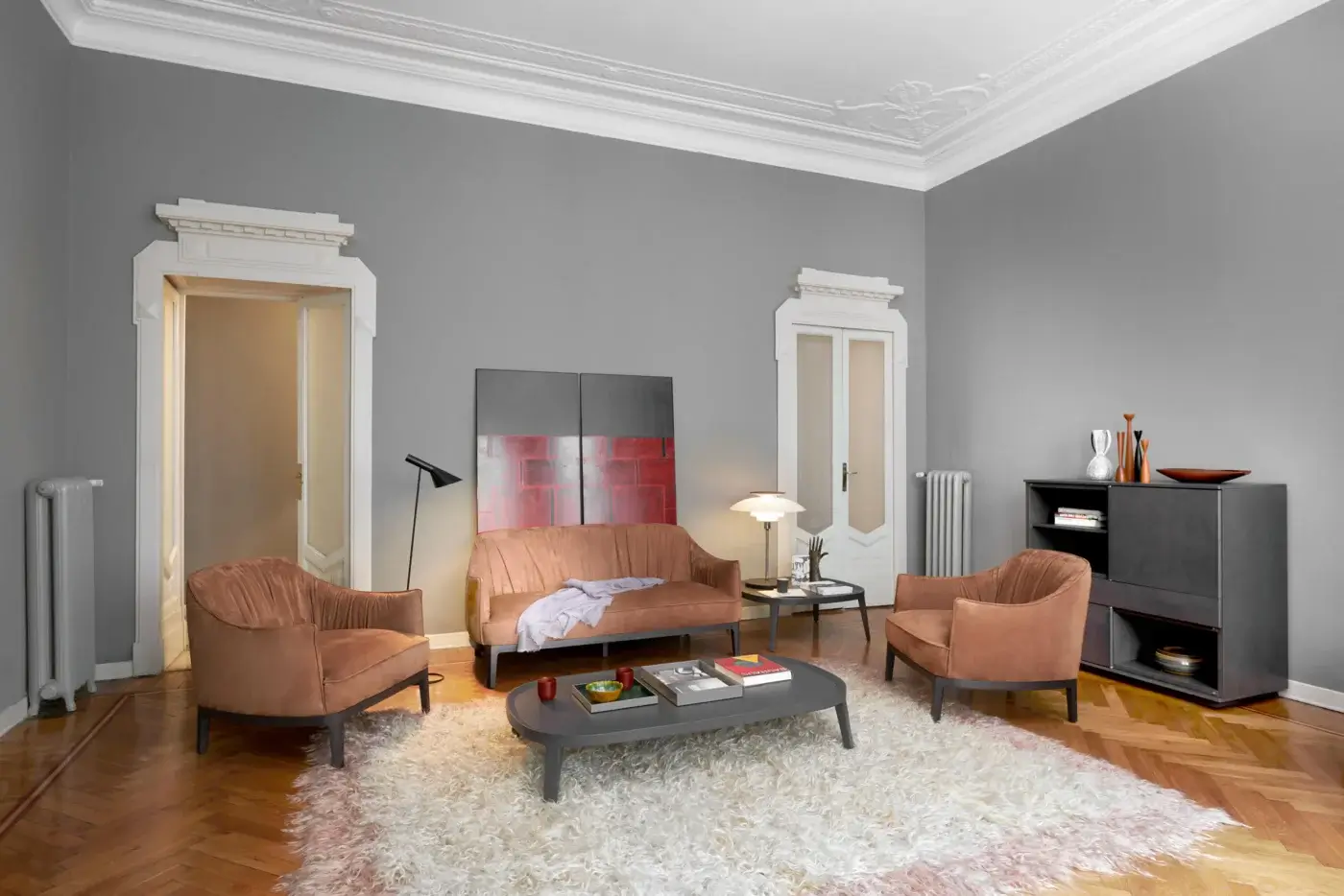 Terracotta velvet sofa with rounded back on off-white shag rug, paired with matching armchairs and dark gray coffee table in a gray living room.