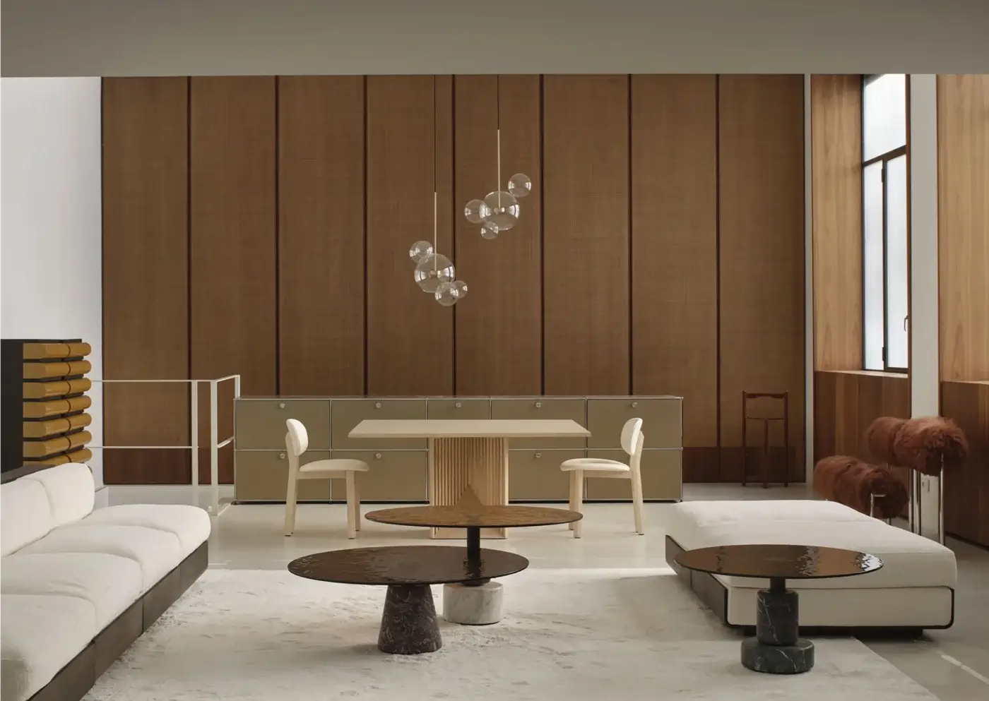 Round Maestro Table with brown wood top and dark cylindrical base in modern living room with beige sofas and wood paneling.