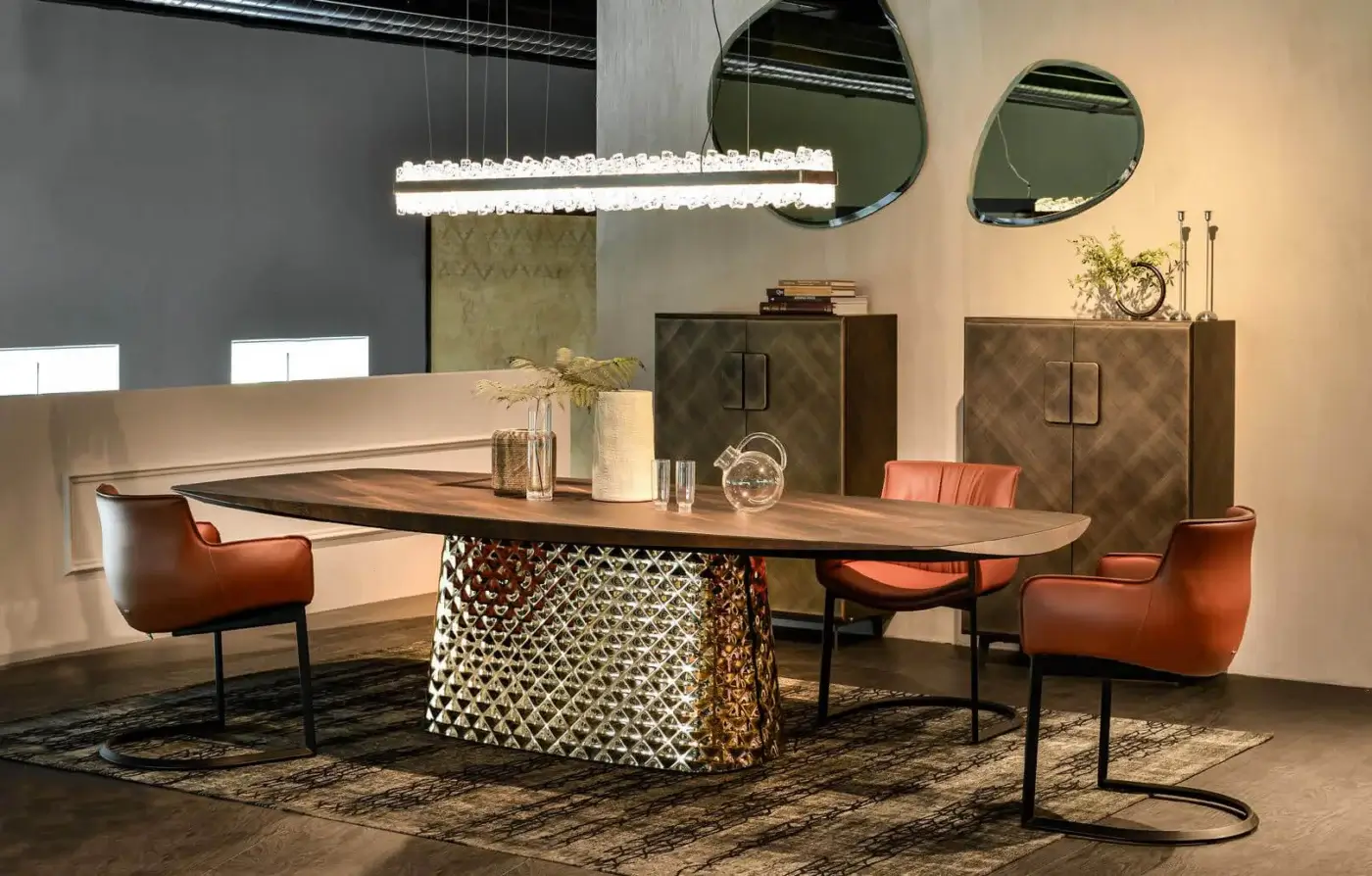 Cattelan Italia Atrium Wood Table, dark wood oval with live edge, geometric gold-toned metal base, surrounded by reddish-brown leather chairs.