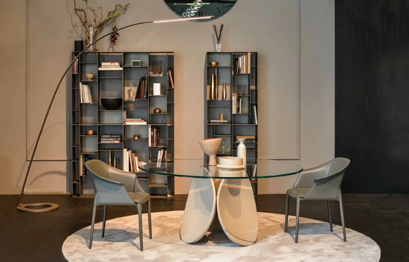 Cattelan Italia Maxim table, beige sculptural base, with gray armchairs, circular rug, and dark gray bookshelves in a modern living room.