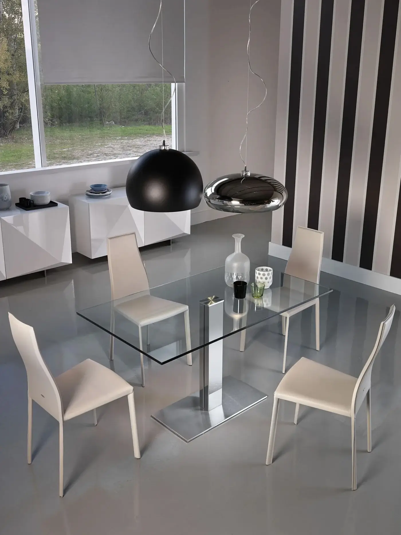 Glass dining table with chrome base, modern chairs, black pendant light, gray walls with black and white striped wallpaper.