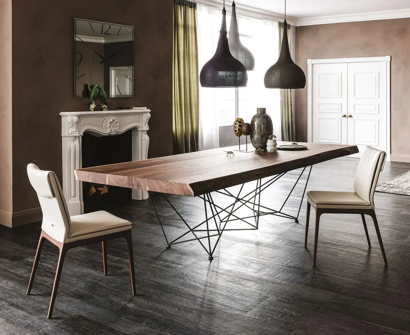 Walnut dining table with live-edge, black metal geometric base, beige leather chairs, pendant lights, marble fireplace, wood flooring.