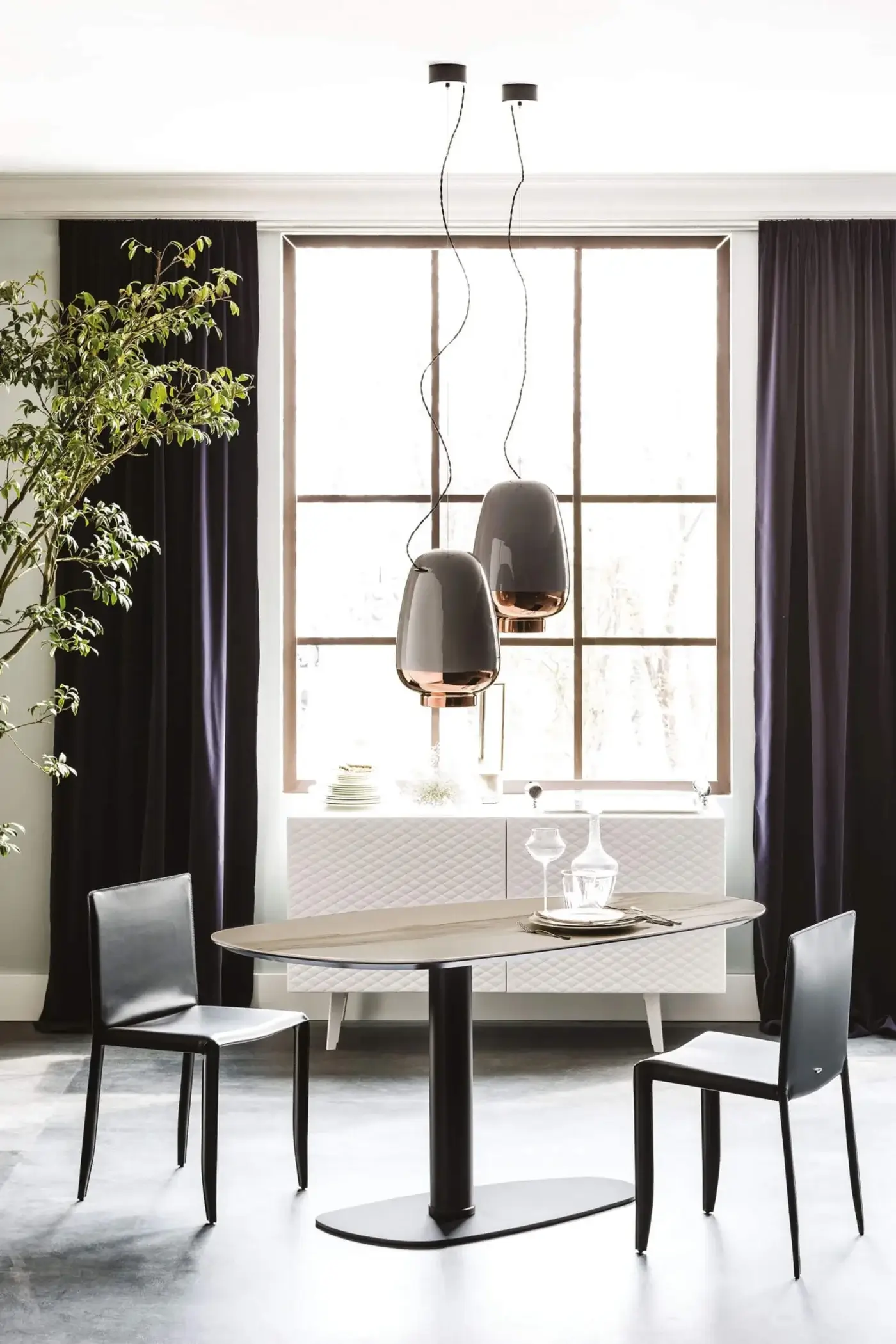 Ipanema ceramic dining table by Cattelan Italia, light gray oval surface, black pedestal base, paired with black chairs and gray pendant lights.