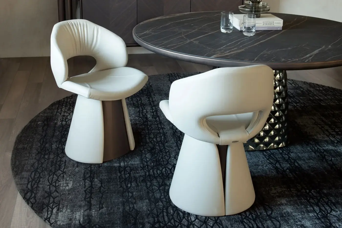 Cattelan Italia dining table, dark gray ceramic top, triangular metal base, paired with light gray sculpted chairs in a modern interior setting.