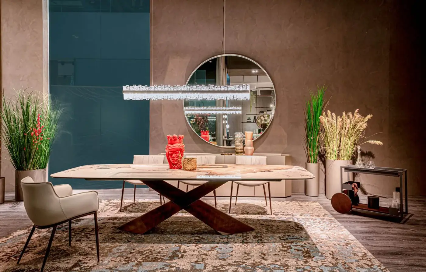 Cattelan Italia Tyron Keramik table with marble-veined top and dark wood X-base, surrounded by gray chairs in a modern teal and brown room.