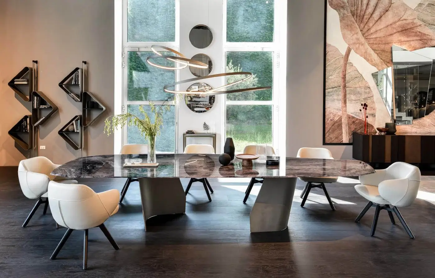 Dining table with dark grey marble top and black flared base, surrounded by six white leather chairs, under a sculptural light fixture.