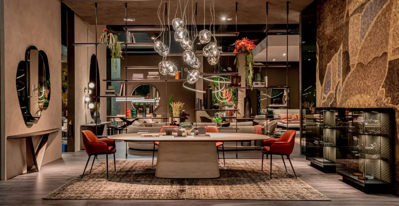 Dining table with light gray ceramic top and dark gray metal base, surrounded by four orange velvet chairs, under a gold chandelier.