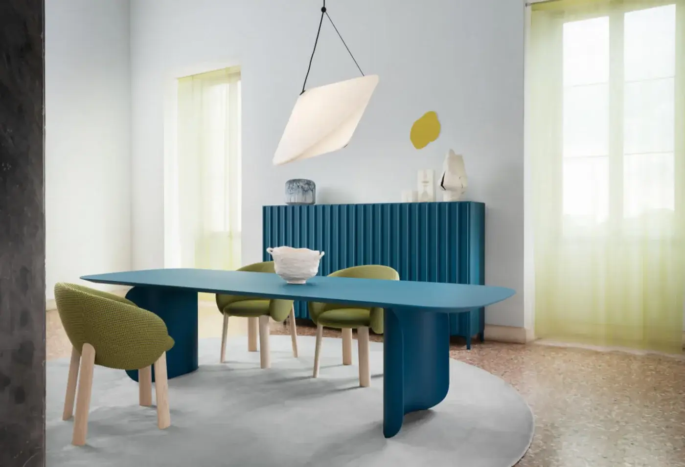 Barry dining table, teal legs, rounded rectangle, paired with green upholstered chairs, gray rug, teal sideboard, and white pendant light.