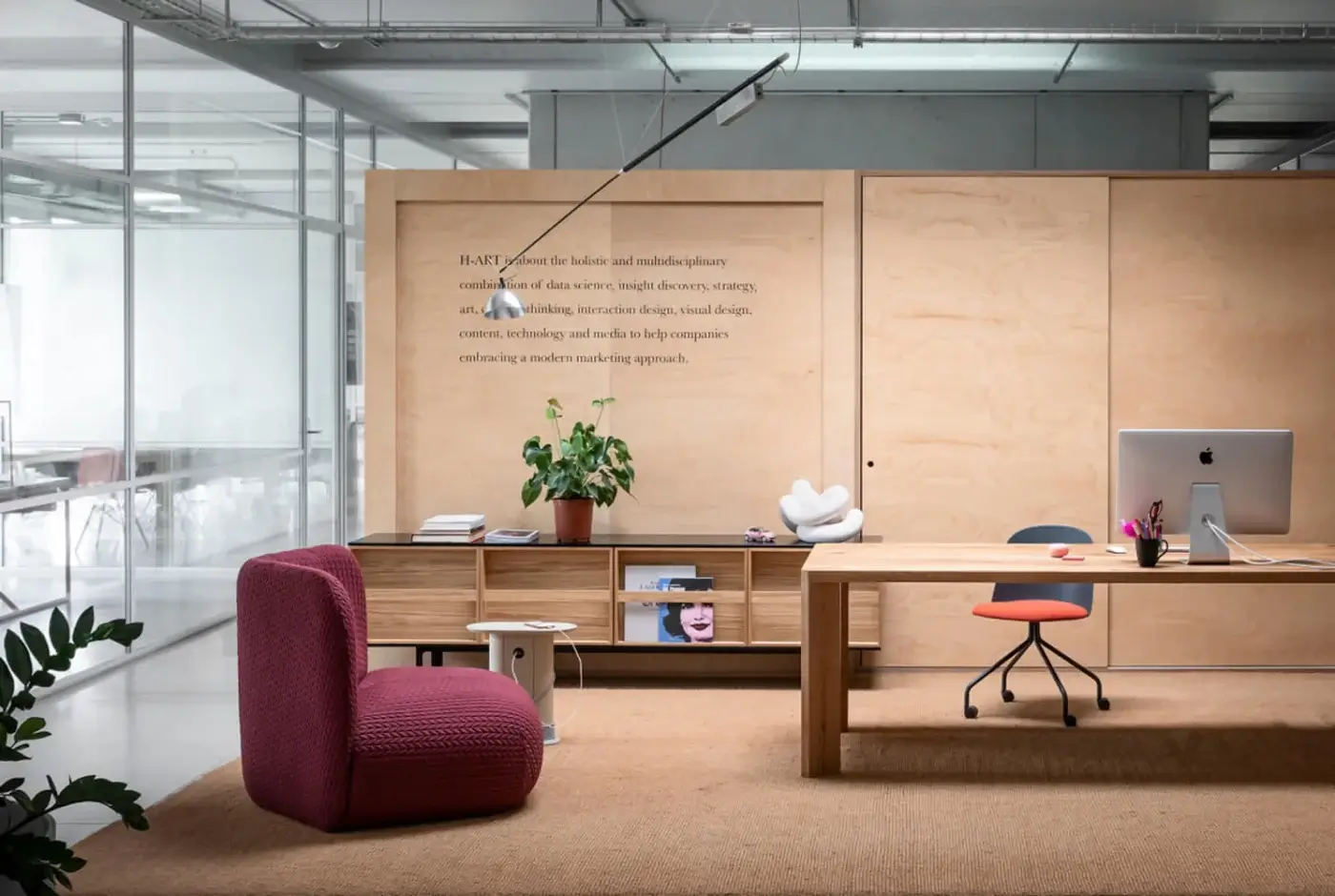 Manero table, light wood and coral-red metal, asymmetrical cantilevered design with integrated storage and drawer, modern workspace scene.