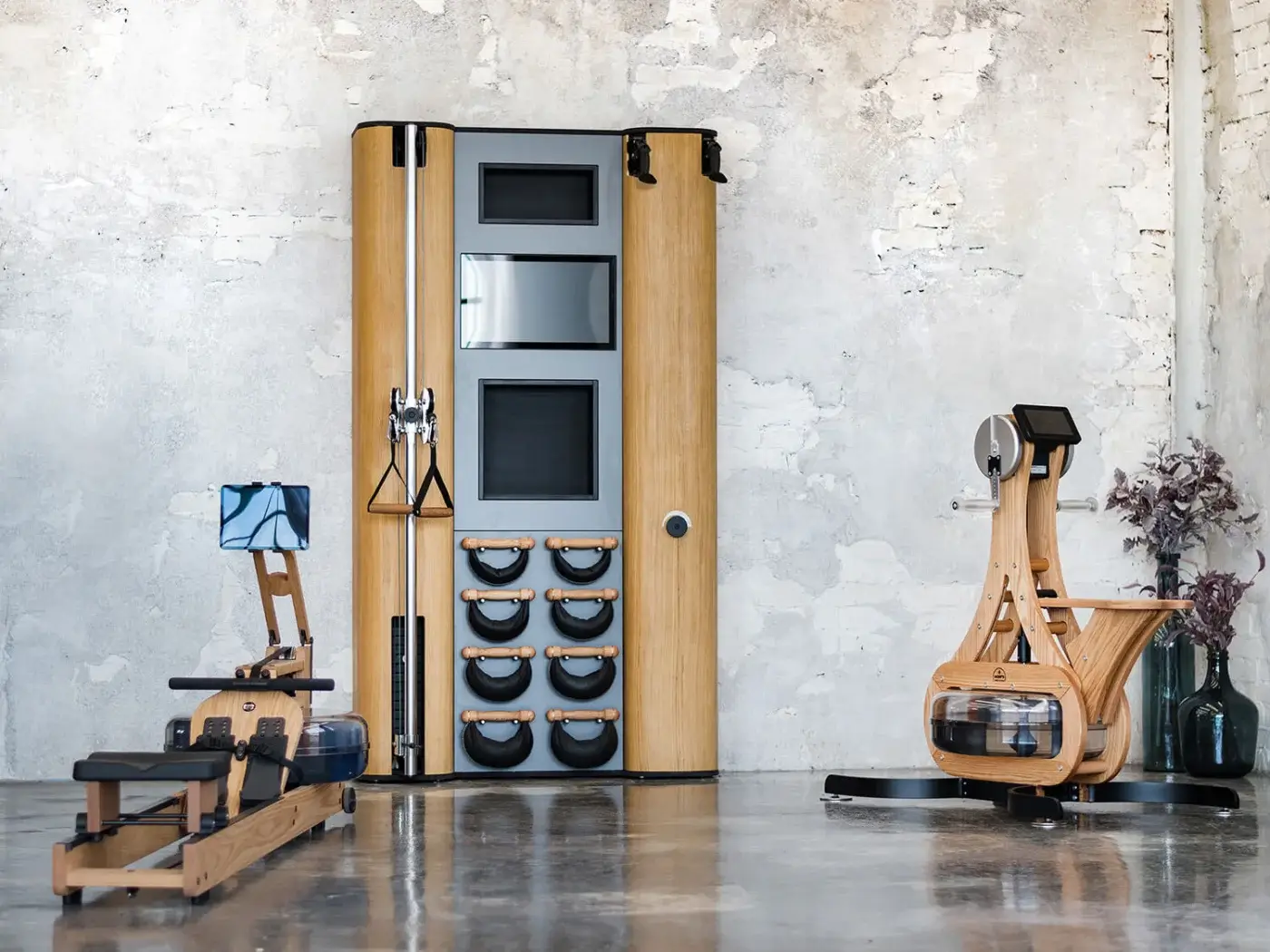 Waterrower showcase, light wood with black accents, features three displays and six resistance band openings, alongside rowing machines on concrete floor.