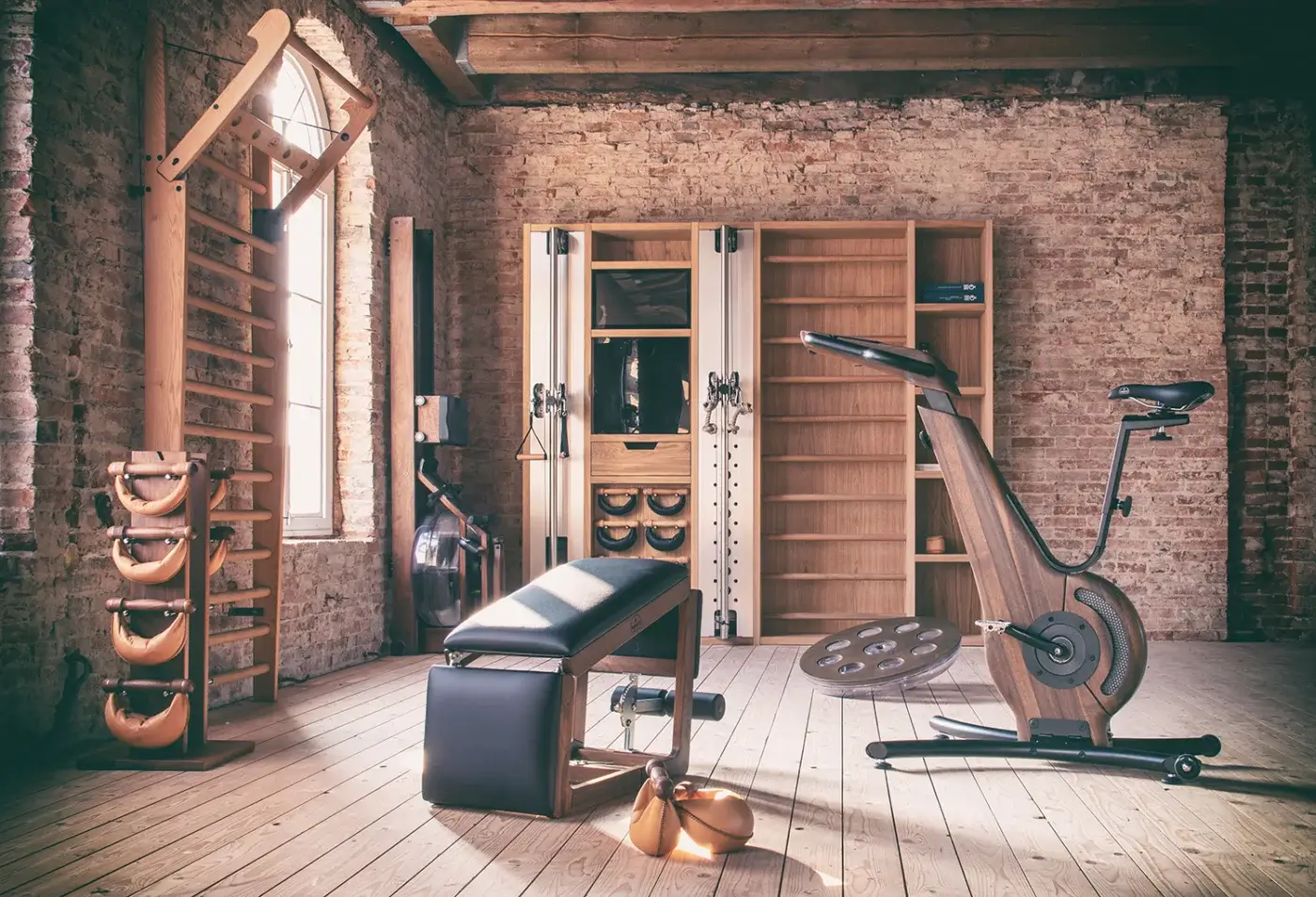Waterrower Nohrd rowing machine, light wood, dark accents, in vintage gym with brick walls, wood floor, exercise equipment, and dumbbells.
