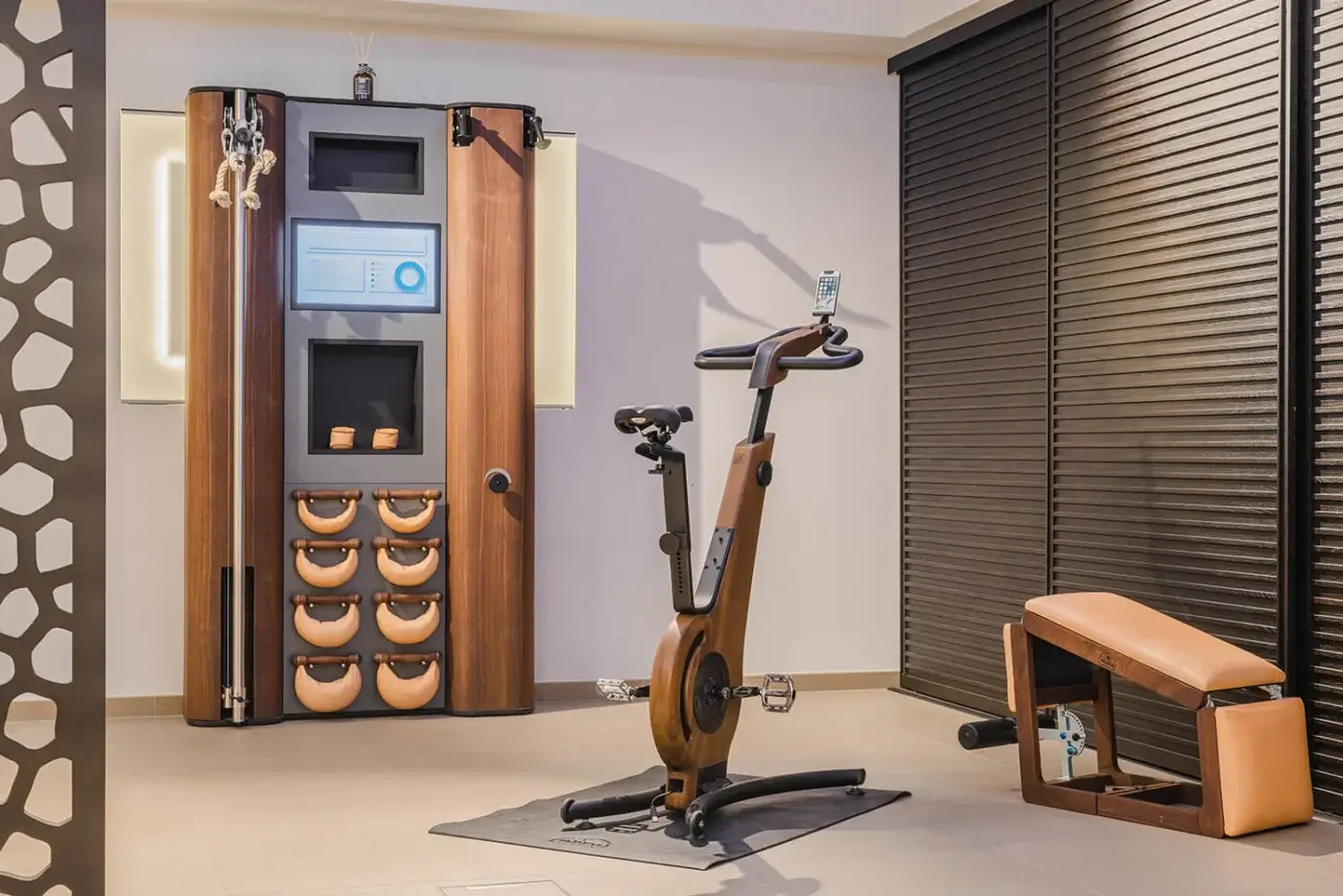 Waterrower Nohrd rowing machine with wooden frame, smartphone mount, and dark wood cabinet with integrated screen in minimalist home gym.