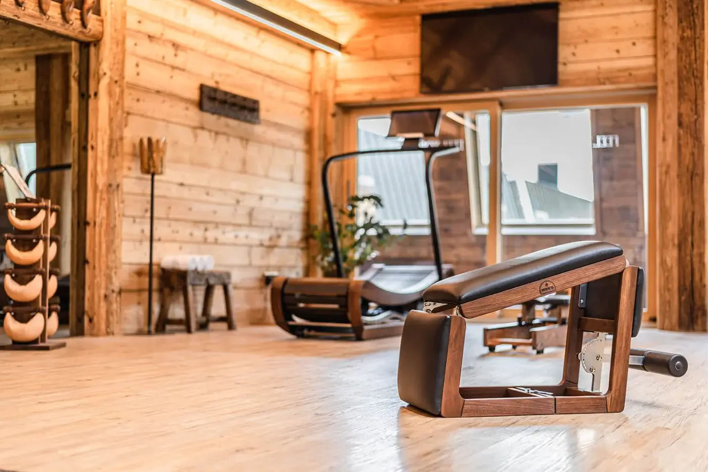 Wood-paneled gym interior with a Waterrower rowing machine, weight bench, dumbbells, and treadmill under warm recessed lighting.