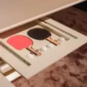 Table tennis table, Vismara, concealed compartment displaying red and black paddles, white balls, beige lining, wood grain edge, interior setting.