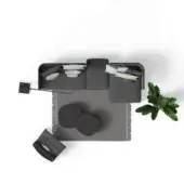 Gray sectional sofa on textured rug with silver tray, green leaves, cushions, and black cylindrical object in a studio setting.