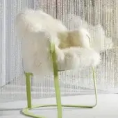 Green metal chair with cream sheepskin throw, curved frame, minimalist design, and clear bead curtain backdrop.