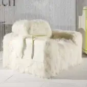 Mongolia Kubrik armchair, cream sheepskin upholstery, boxy silhouette with rounded arms, gold metal side table, silver strand backdrop.