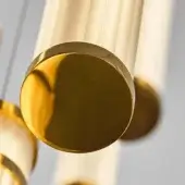 Polished brass cylindrical lighting fixture with sandblasted texture and rounded caps, suspended against a light gray backdrop.