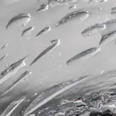 Diamond plate metal surface, silver tone, with repeating raised elongated diamond shapes and reflective light patterns creating a rippling effect.