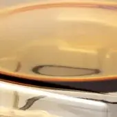 Ambra tau tabletop, golden-beige polished surface, circular form with dark liquid pooling, white angular edge, reflective center.