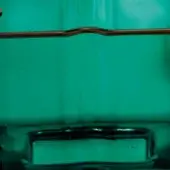 Teal curtain fabric with vertical folds partially covers a dark reflective frame, beneath a curved wooden rod; text reads "smeraldo tau".