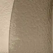 Textured wall segment with bronzo and sand-colored mottled finish, uneven granular surface, and shadowed depth suggesting rustic plaster construction.