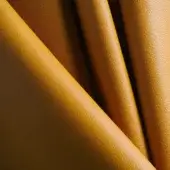 Mustard yellow leather texture with a pebbled grain, displaying sharp diagonal folds and matte finish, highlighted by directional lighting.