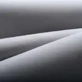 Gray fabric texture with matte finish, displaying soft folds and uniform grain, creating overlapping planes and subtle light-shadow variations.