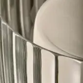 Satin white carved plates stacked in overlapping arrangement, displaying intricate vertical ridges and a transparent layered effect in studio lighting.