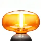 Crystal table lamp with amber rounded shade, exposed filament bulb, dark matte base, and chain suspension against a white backdrop.