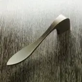 Bronze door handle with elongated, curved design and brushed finish displayed against dark gray wood grain texture.