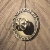 Brass door handle, circular shape with clover-like knob, mounted on a diagonally-grained brown wood door, featuring scalloped detailing.