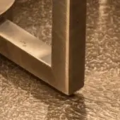 Brass furniture frame detail, hammered cast brass finish, square legs with etched “31”, warm golden hue, studio lighting.