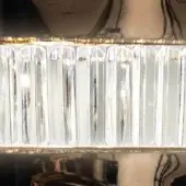 Crystal linear light fixture with fluted rectangular elements, warm yellow illumination, metallic mounting band, and vertical arrangement.