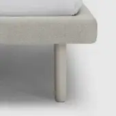 Bed feet, light gray herringbone upholstery, cylindrical light beige legs, studio shot, white fitted sheet, tapered design.