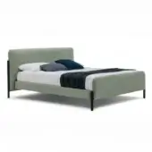 Sage green upholstered bed with flag footboard, black metal frame, white linens, navy and white pillows, studio shot.