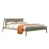 Bed with light wood frame, woven headboard, and white linen bedding, accented by an orange throw blanket and cream pillows.