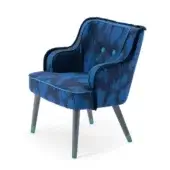 Blue velvet armchair with profile fringe, turquoise trim, curved back, and dark gray legs with teal accents, against a white backdrop.