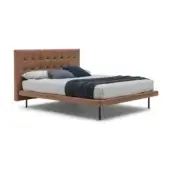 Tan leather tufted bed with low platform, black metal legs, gray linen duvet, and blue throw, labeled “freedom – h.9 base”.